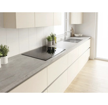 Cuisine moderne lumineuse avec plan de travail aspect béton, plaque à induction, meubles sans poignées et évier en acier inoxydable.