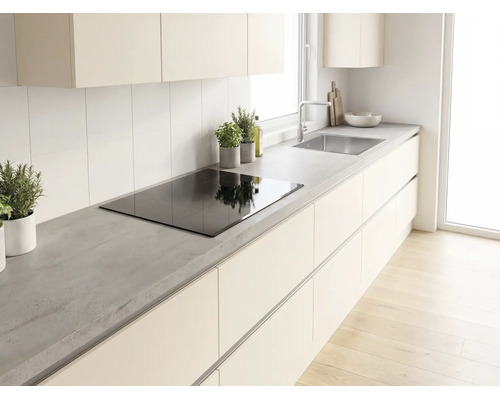 Cuisine moderne lumineuse avec plan de travail aspect béton, plaque à induction, meubles sans poignées et évier en acier inoxydable.