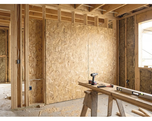 Intérieur de bâtiment brut lumineux avec panneaux OSB sur ossature bois, isolation et établi organisé avec perceuse, marteau et niveau à bulle.