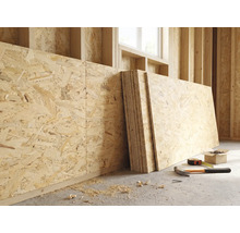 Panneaux OSB contre un mur en bois dans un chantier lumineux avec marteau, mètre ruban et vis au sol.