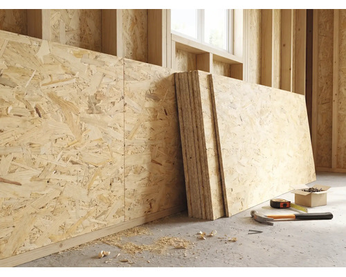 Panneaux OSB contre un mur en bois dans un chantier lumineux avec marteau, mètre ruban et vis au sol.