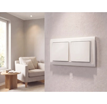 Interrupteur double moderne blanc sur un mur texturé dans un salon lumineux avec fauteuil et petite table.