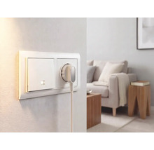 Lichtschalter und Steckdose mit flachem Stecker an einer Wand in einem hellen, modern eingerichteten Wohnzimmer.