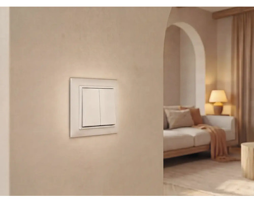 Zweifacher Wippschalter an einer hellen Wand in einem modern eingerichteten Wohnzimmer mit Sofa und Lampe.