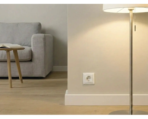 Moderne Wohnzimmerszene mit einer weißen Steckdose an der Wand, einer Stehleuchte, Holzboden und einem grauen Sofa im Hintergrund.