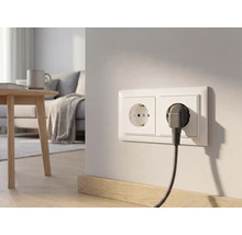 Double prise de courant sur un mur clair dans un salon moderne avec une fiche branchée et un câble tressé.