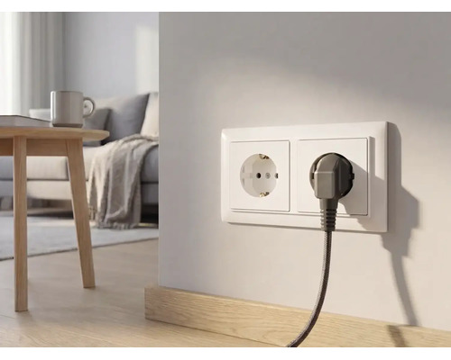 Double prise de courant sur un mur clair dans un salon moderne avec une fiche branchée et un câble tressé.