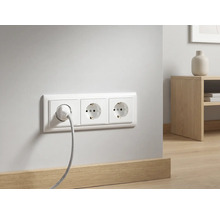 Triple prise de courant murale avec un câble branché sur un mur blanc au-dessus d'une plinthe en bois dans une pièce moderne.