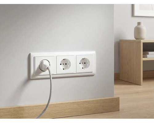 Triple prise de courant murale avec un câble branché sur un mur blanc au-dessus d'une plinthe en bois dans une pièce moderne.