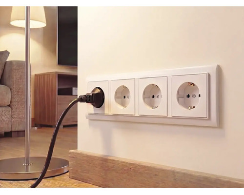 Prise murale quadruple avec terre sur un mur clair dans un salon avec une fiche noire branchée pour un lampadaire.