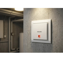 Weißer Heizungsschalter mit Aufdruck Heizung und roter Kontrollleuchte an einer Betonwand im Keller.