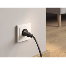 Schwarzer Schukostecker in weißer Wandsteckdose in einem hellen Raum mit Holzboden.
