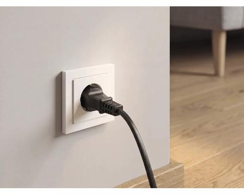 Schwarzer Schukostecker in weißer Wandsteckdose in einem hellen Raum mit Holzboden.