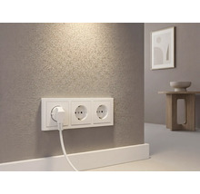 Dreifach-Steckdose mit eingestecktem Stecker an einer strukturierten Wand in einem hellen Raum.