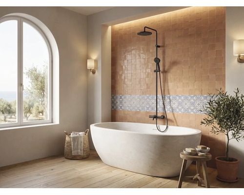 Salle de bains lumineuse avec baignoire en îlot, système de douche noir, carrelage mural et grande fenêtre cintrée.