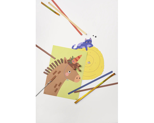 Projet de bricolage avec un cheval en papier, un chat sur une botte de foin, des bandes de papier colorées et des outils.