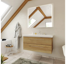 Salle de bains moderne avec meuble sous-vasque en chêne, lavabo blanc et miroir éclairé sous un toit en pente avec poutres en bois.