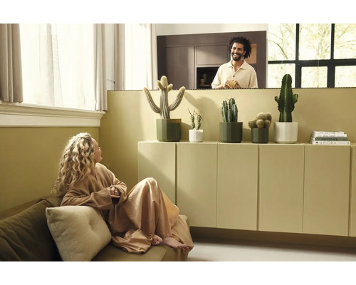 Salon moderne et lumineux avec des cactus en pots sur un buffet, une femme sur un canapé et un homme à l'arrière-plan.