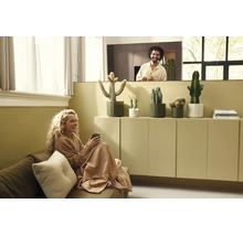 Salon lumineux avec une femme sur le canapé et un homme derrière une cloison. Cactus en pots posés sur un meuble minimaliste.