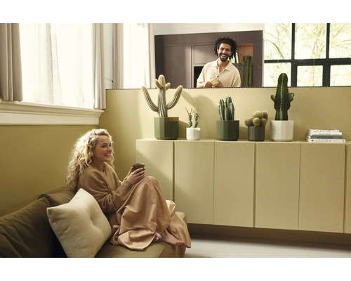 Salon lumineux avec une femme sur le canapé et un homme derrière une cloison. Cactus en pots posés sur un meuble minimaliste.