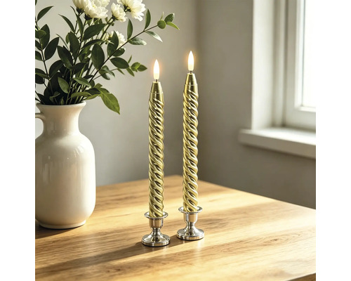 Zwei gedrehte LED-Stabkerzen in Gold auf silbernen Kerzenständern auf einem Holztisch neben einer weißen Vase mit Blumen.