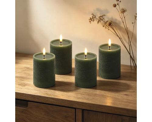 Vier grüne LED-Stumpenkerzen mit Struktur auf einer Holzkommode mit Trockenblumen dekoriert.
