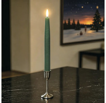 Grüne LED-Stabkerze mit beweglicher Flamme in silbernem Kerzenständer auf einem dunklen Tisch in einem Wohnzimmer.