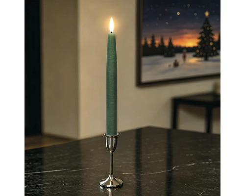 Grüne LED-Stabkerze mit beweglicher Flamme in silbernem Kerzenständer auf einem dunklen Tisch in einem Wohnzimmer.