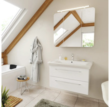 Salle de bains avec meuble sous-lavabo blanc, lavabo en céramique et armoire de toilette à trois portes avec éclairage dans des combles clairs.