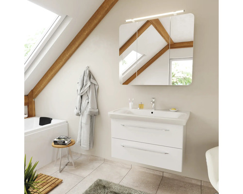 Salle de bains avec meuble sous-lavabo blanc, lavabo en céramique et armoire de toilette à trois portes avec éclairage dans des combles clairs.