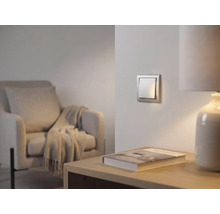 Interrupteur à bascule argenté moderne au mur dans un salon lumineux avec un fauteuil et une lampe de table.
