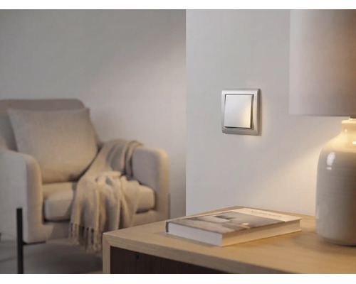Interrupteur à bascule argenté moderne au mur dans un salon lumineux avec un fauteuil et une lampe de table.