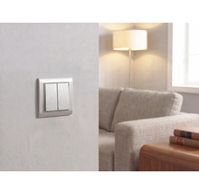 Interrupteur double moderne sur un mur dans un salon lumineux avec canapé, lampadaire et table en bois.
