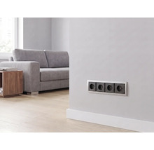 Prise quadruple installée sur un mur dans un salon moderne et lumineux avec canapé et parquet.