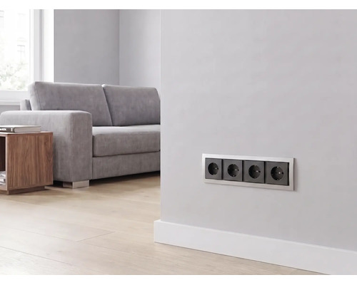 Prise quadruple installée sur un mur dans un salon moderne et lumineux avec canapé et parquet.
