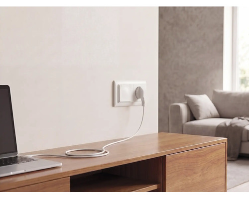 Prise murale avec fiche et câble connectés à un ordinateur portable sur un buffet en bois dans un salon lumineux.