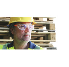 Ouvrier avec casque de chantier jaune et lunettes de protection devant des palettes en bois empilées.