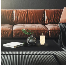 Modernes Wohnzimmer mit Ledersofa, strukturiertem Couchtisch, kleiner Dekolampe, Vase mit Pflanze und Buch vor dunkler Wand.