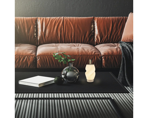 Modernes Wohnzimmer mit Ledersofa, strukturiertem Couchtisch, kleiner Dekolampe, Vase mit Pflanze und Buch vor dunkler Wand.