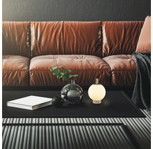 Modernes Wohnzimmer mit braunem Ledersofa, schwarzem Couchtisch und kleiner, leuchtender kugelförmiger Tischleuchte mit Tragegriff.