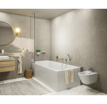 Salle de bains moderne et lumineuse avec baignoire blanche, bidet suspendu, meuble sous-vasque en bois, miroir rond et carrelage mural gris.