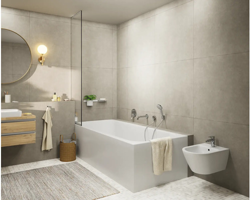 Salle de bains moderne et lumineuse avec baignoire blanche, bidet suspendu, meuble sous-vasque en bois, miroir rond et carrelage mural gris.