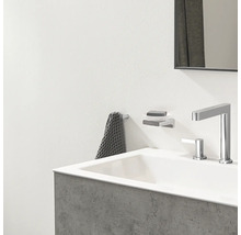 Modernes Badezimmer mit weißem Waschbecken, verchromter Armatur, Seifenhalter zur Wandmontage und grauem Handtuch an einem Haken.