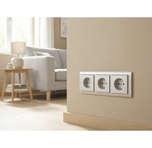 Triple prise de courant avec terre installée dans un salon moderne et clair avec canapé et table d'appoint.