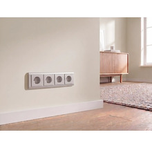 Prise électrique quadruple installée sur un mur au-dessus d'une plinthe dans une pièce moderne et lumineuse.
