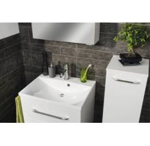 Salle de bain moderne avec meuble sous-lavabo blanc, lavabo et armoire latérale sur fond de carrelage mural sombre texturé.