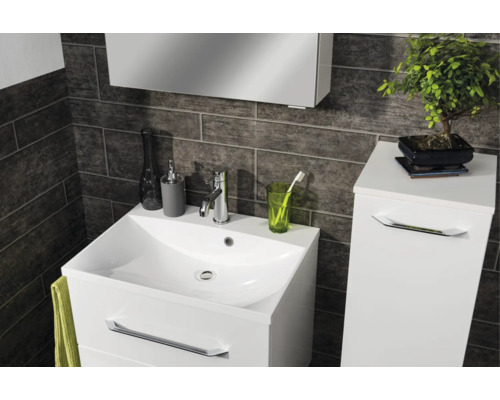 Salle de bain moderne avec meuble sous-lavabo blanc, lavabo et armoire latérale sur fond de carrelage mural sombre texturé.
