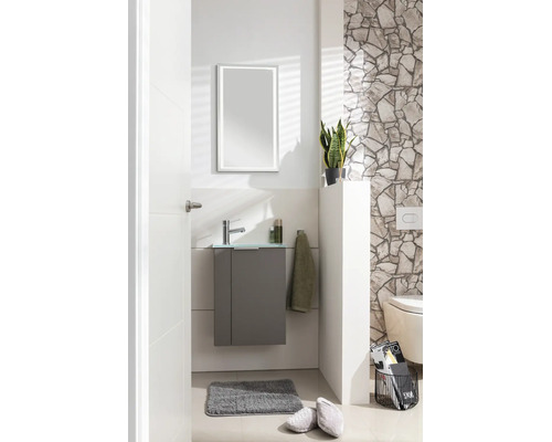 Toilettes d'invités modernes avec meuble gris sous-lavabo, vasque en verre, robinetterie chromée et miroir LED devant un mur en pierre naturelle.
