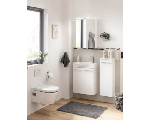 Salle de bains lumineuse avec meuble sous-lavabo blanc, WC suspendu, armoire de toilette et colonne de rangement sur sol en bois clair.