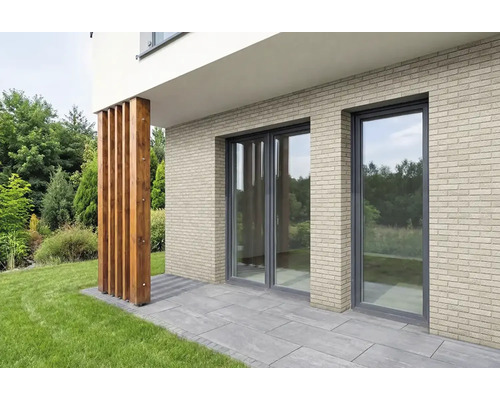 Fassade mat hellen Verblendsteine mat Klinkeroptik, gliesene Fronten an enger Terrass mat groe Steenplacken.